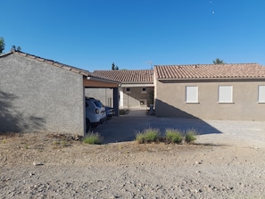 A residential building with a covered garage, a gravel driveway, and a clear blue sky.
