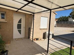 Un espace extérieur abrité, doté d’une porte, d’une fenêtre, d’un petit climatiseur et d’une rambarde en métal.