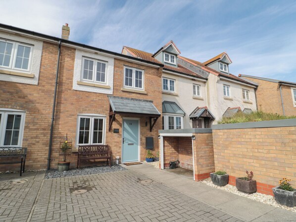 A row of terraced houses with a paved courtyard, a bench, and potted plants. - Brucap Cottage (Chathill)