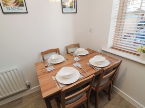 A dining table set with white plates, bowls, and cutlery, surrounded by wooden chairs. - Brucap Cottage (Chathill)