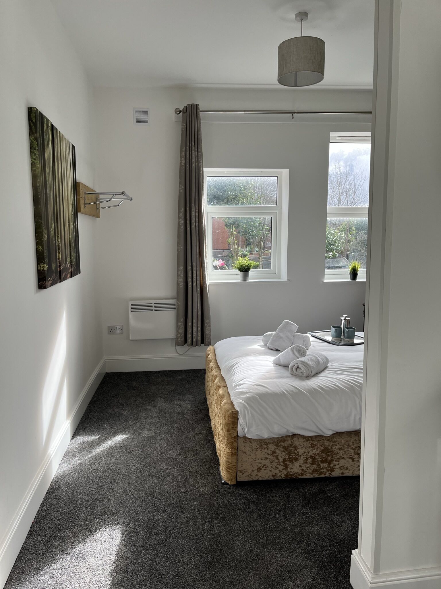 A bedroom with a bed, a window with curtains, a radiator, and a wall-mounted artwork.