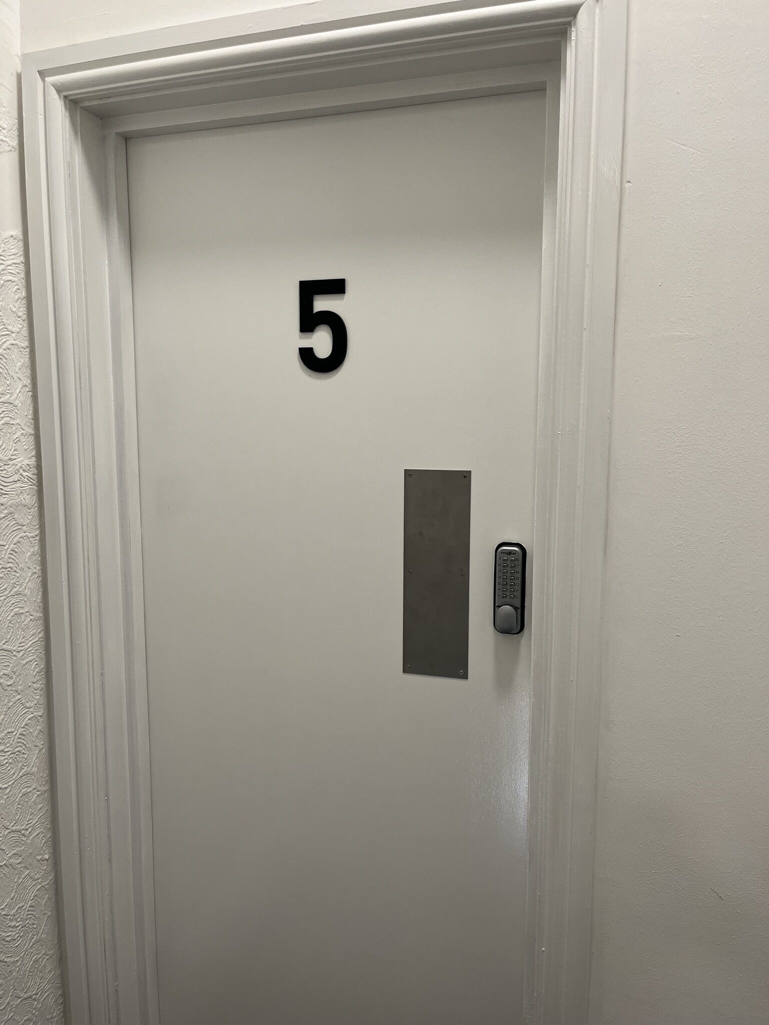 A white door with the number 5, a keypad lock, and a small rectangular panel.
