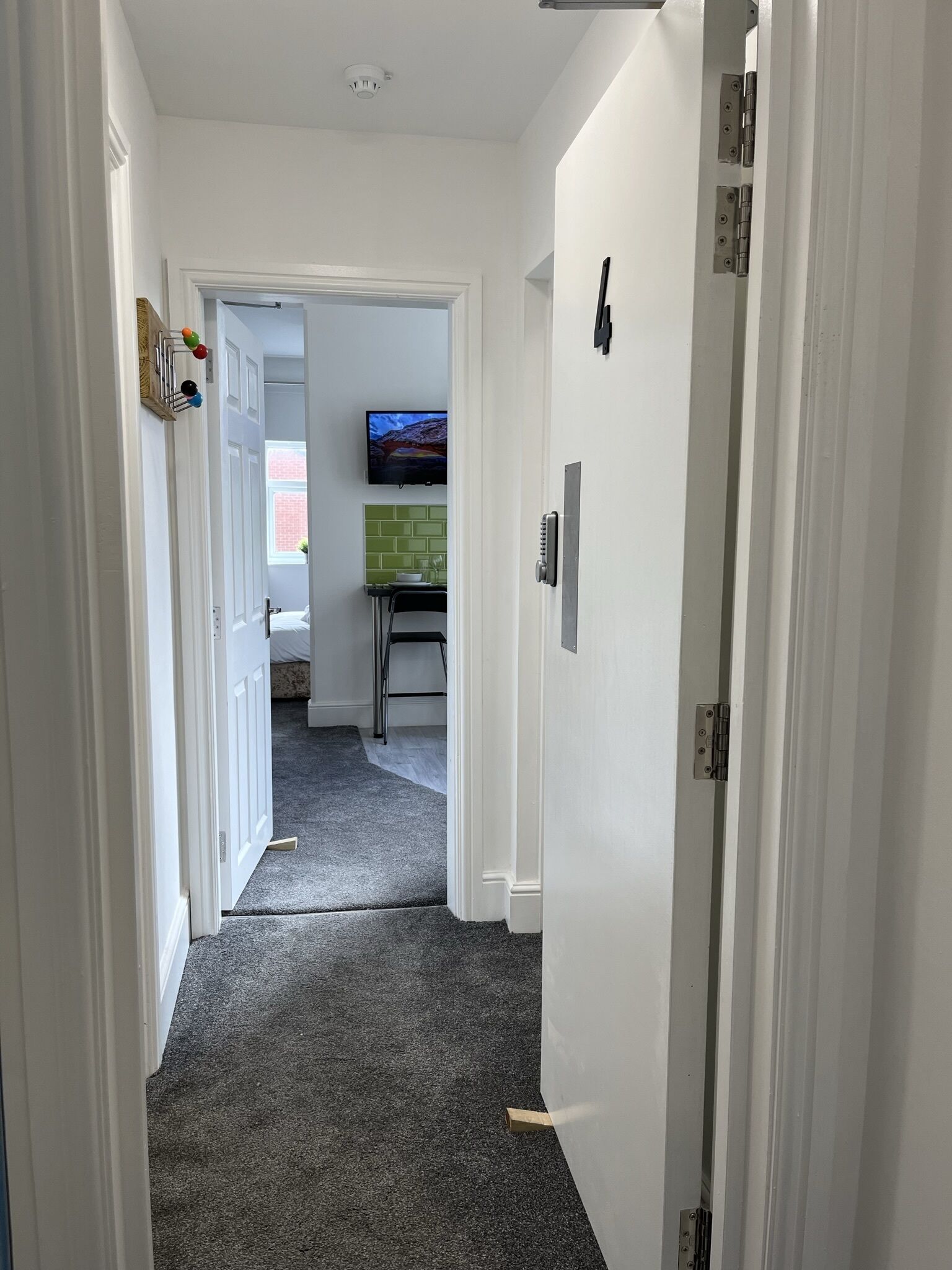En smal hall med ett heltäckningsmatta som leder till ett rum med en tv och en grön kakelvägg bakom tv:n.