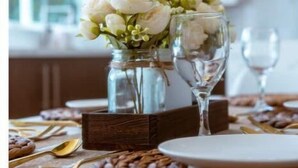 Een eettafel gedekt met witte borden, gouden bestek en een vaas witte bloemen.