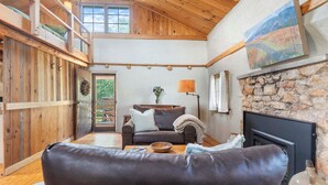 A cozy living room with a high ceiling, wooden walls, a stone fireplace, and a large window. - Rustic Bailey's Retreat Cabin Near Wineries! (Charlottesville)