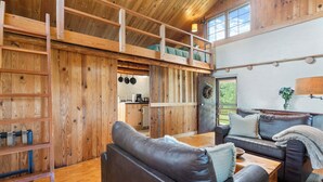 A spacious loft-style room with a wooden interior, a loft bed, a dining area, and a kitchen in the background. - Rustic Bailey's Retreat Cabin Near Wineries! (Charlottesville)