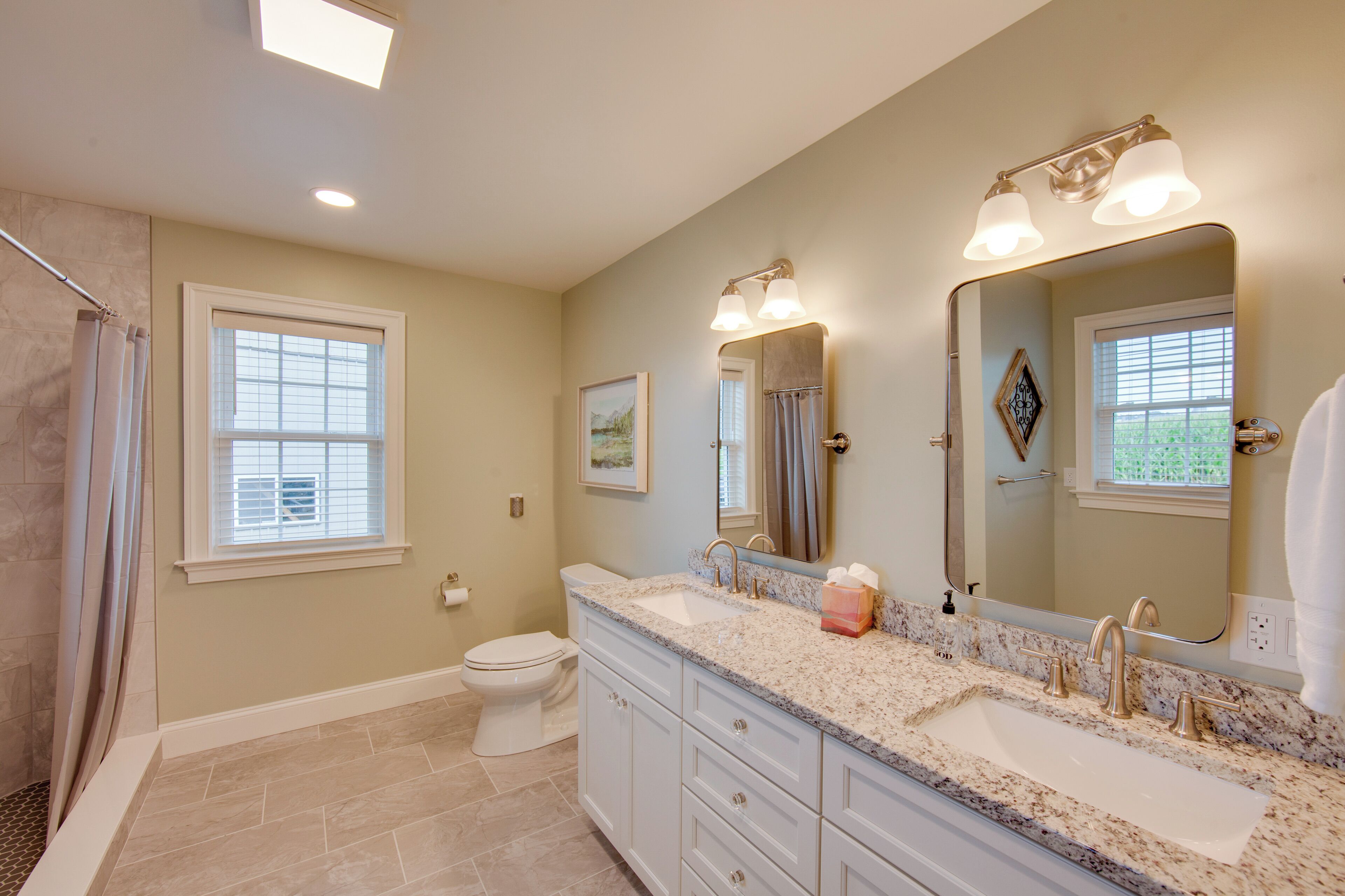 A bathroom with a large vanity, a double sink, a toilet, and a shower area.