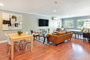 A modern living room with a wooden dining table, a sofa, and a flat-screen TV mounted on the wall. - Toledo Vacation Rental ~ 5 Mi to Downtown! (Toledo)