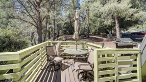 A wooden deck with a glass table and chairs, surrounded by a green fence and trees. - Modern Pine Mountain Club Cabin w/ Community Pool! (Pine Mountain Club)