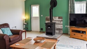Un salon avec un canapé en cuir marron, une table basse en bois, un téléviseur posé sur un meuble en bois et un poêle à bois noir.