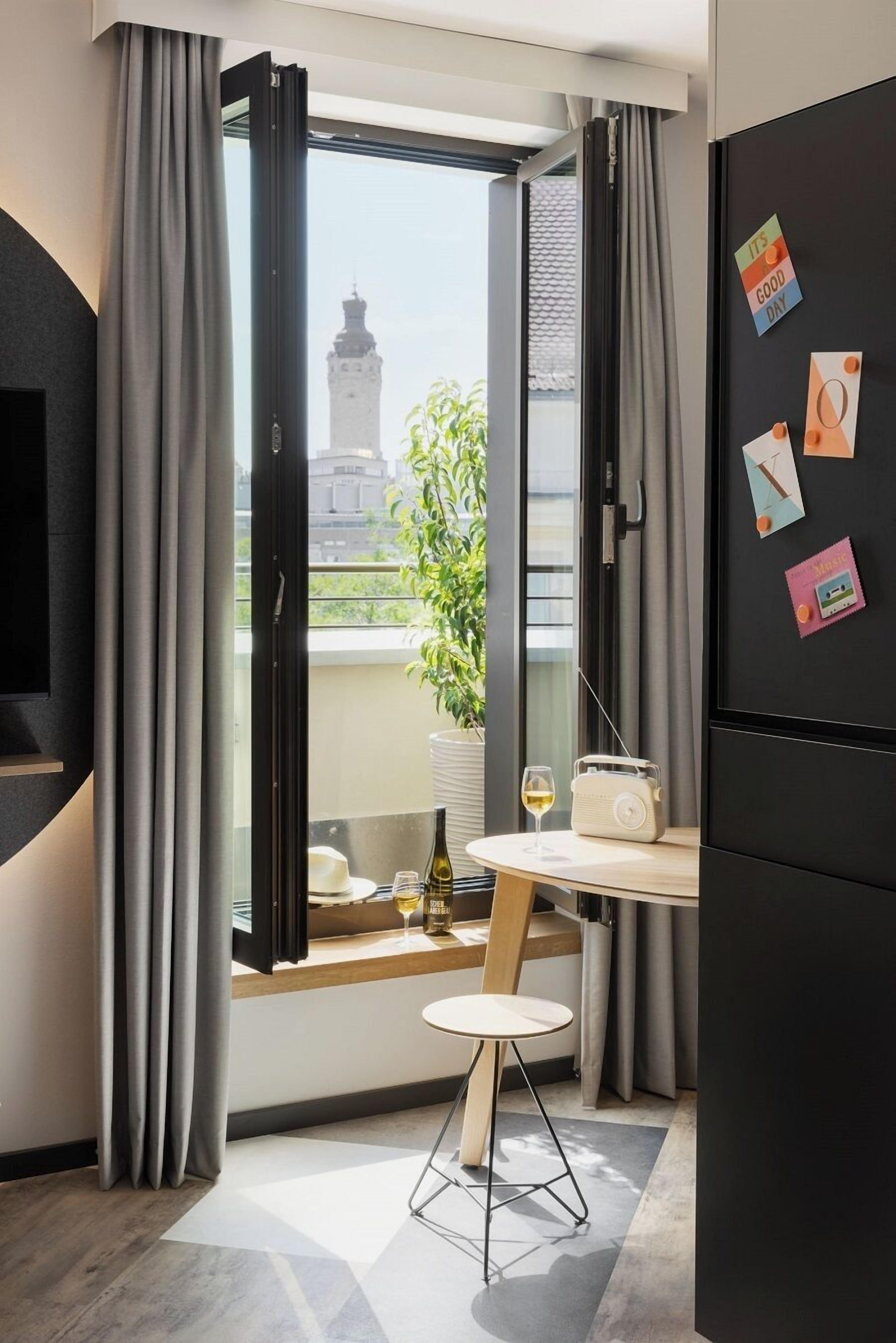 A modern room with a large window, a table with a radio and wine glass, and a view of a building outside.