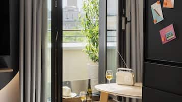 Una habitación moderna con un ventanal grande, una mesa con un radio y una copa de vino, y vistas a un edificio.