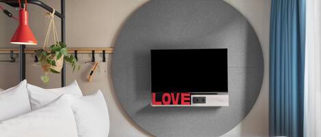 Una habitación de hotel moderna con una cama grande, un televisor montado, una lámpara colgante roja y un adorno circular en la pared con la palabra 'LOVE'.