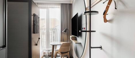 A compact hotel room with a dining area, a TV mounted on the wall, and a guitar hanging on the wall.