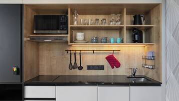 A compact kitchen with a microwave, oven, and sink. There are shelves with dishes and glasses, and a red oven mitt hanging.