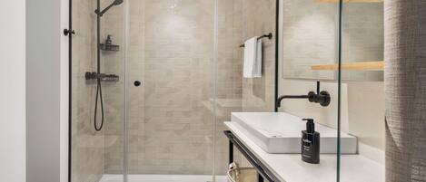 A modern bathroom with a glass-enclosed shower, a white sink, and a wooden shelf.