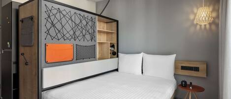 Une chambre à coucher moderne avec un lit, une petite table de chevet, une étagère fixée au mur et un luminaire suspendu.