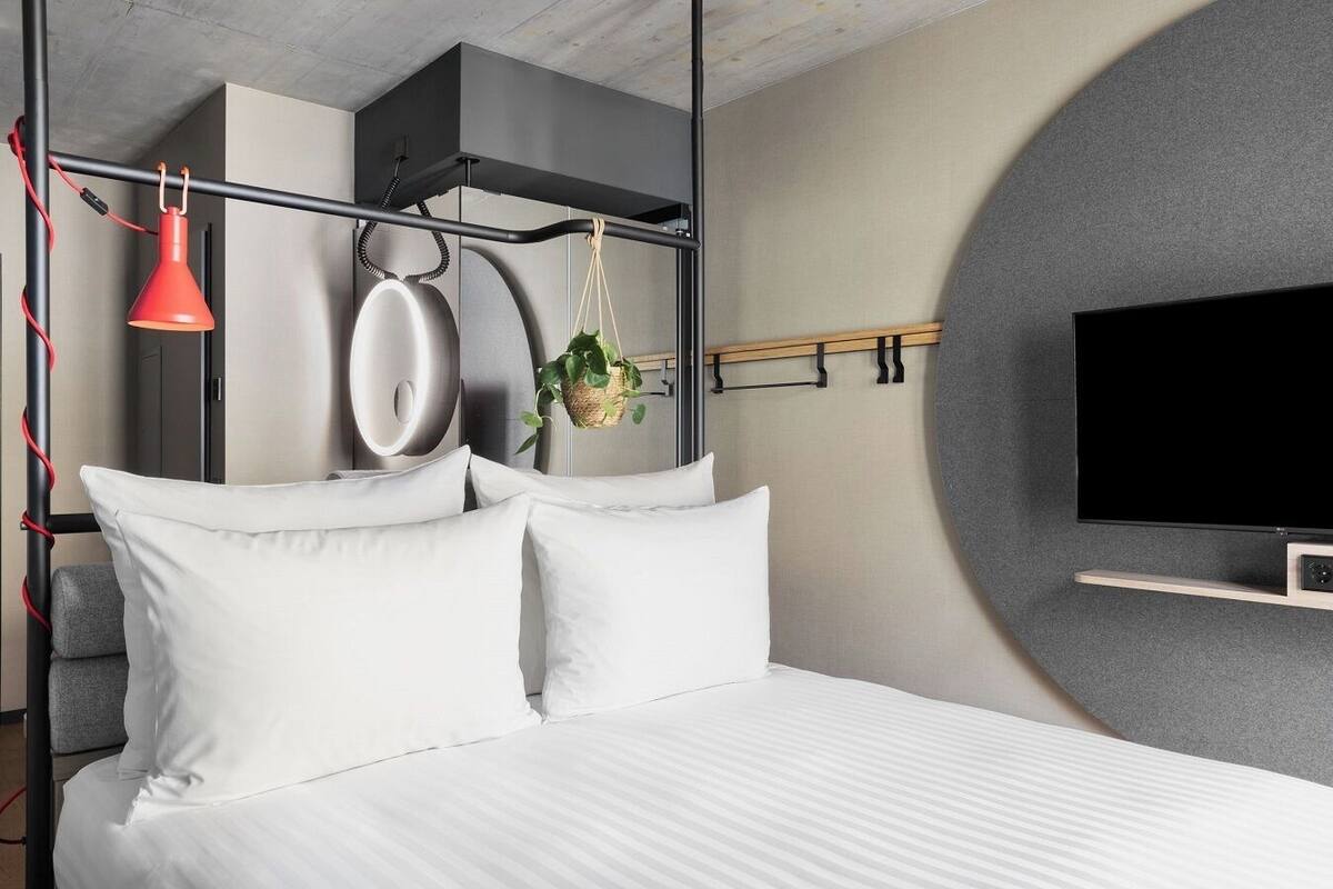 A modern bedroom with a bed, white pillows, a red lamp, a TV, and a circular wall feature.
