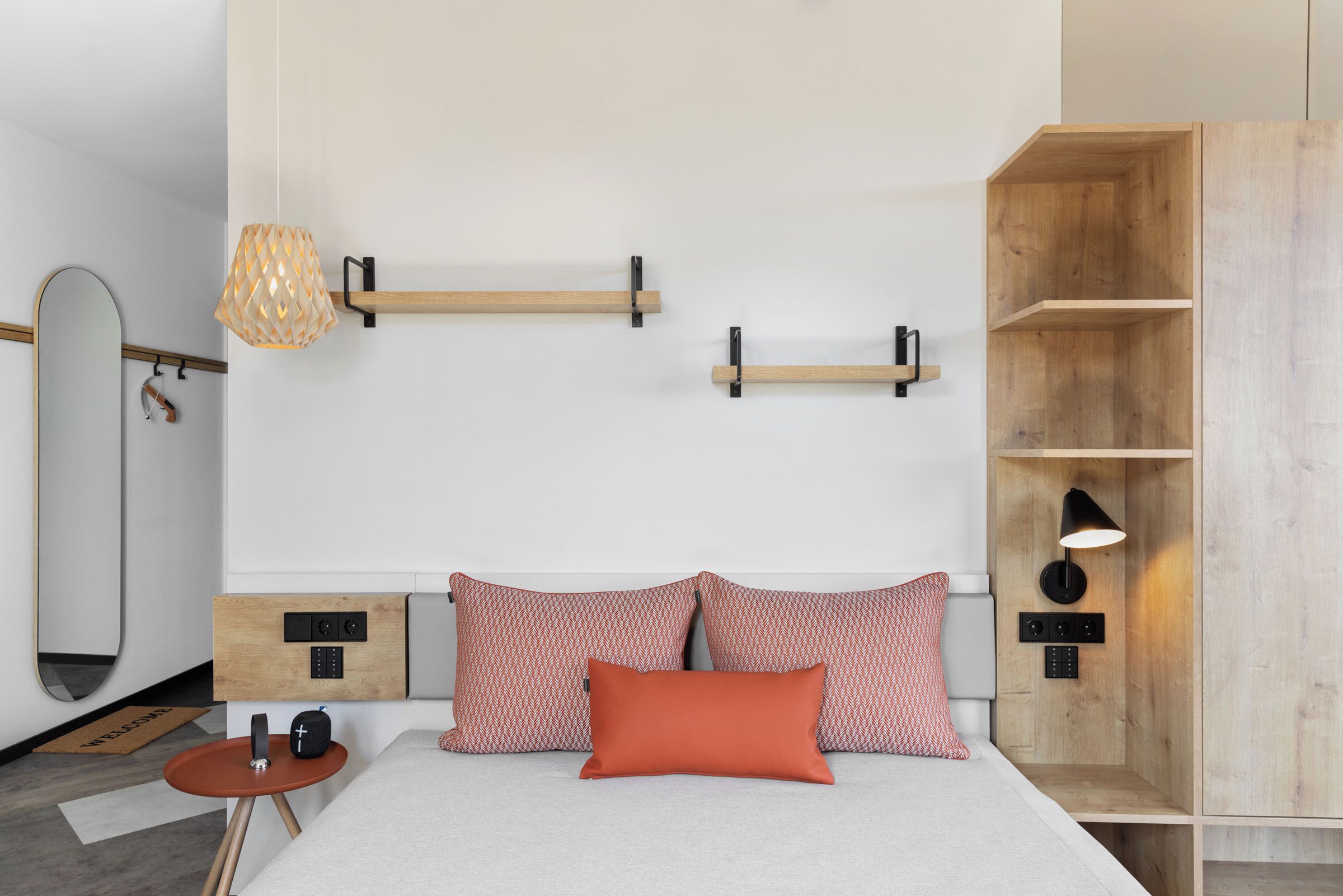 A modern bedroom with a bed, bedside tables, a mirror, and built-in shelves.