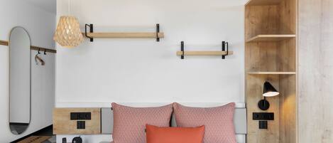 A modern bedroom with a bed, bedside tables, a mirror, and built-in shelves.