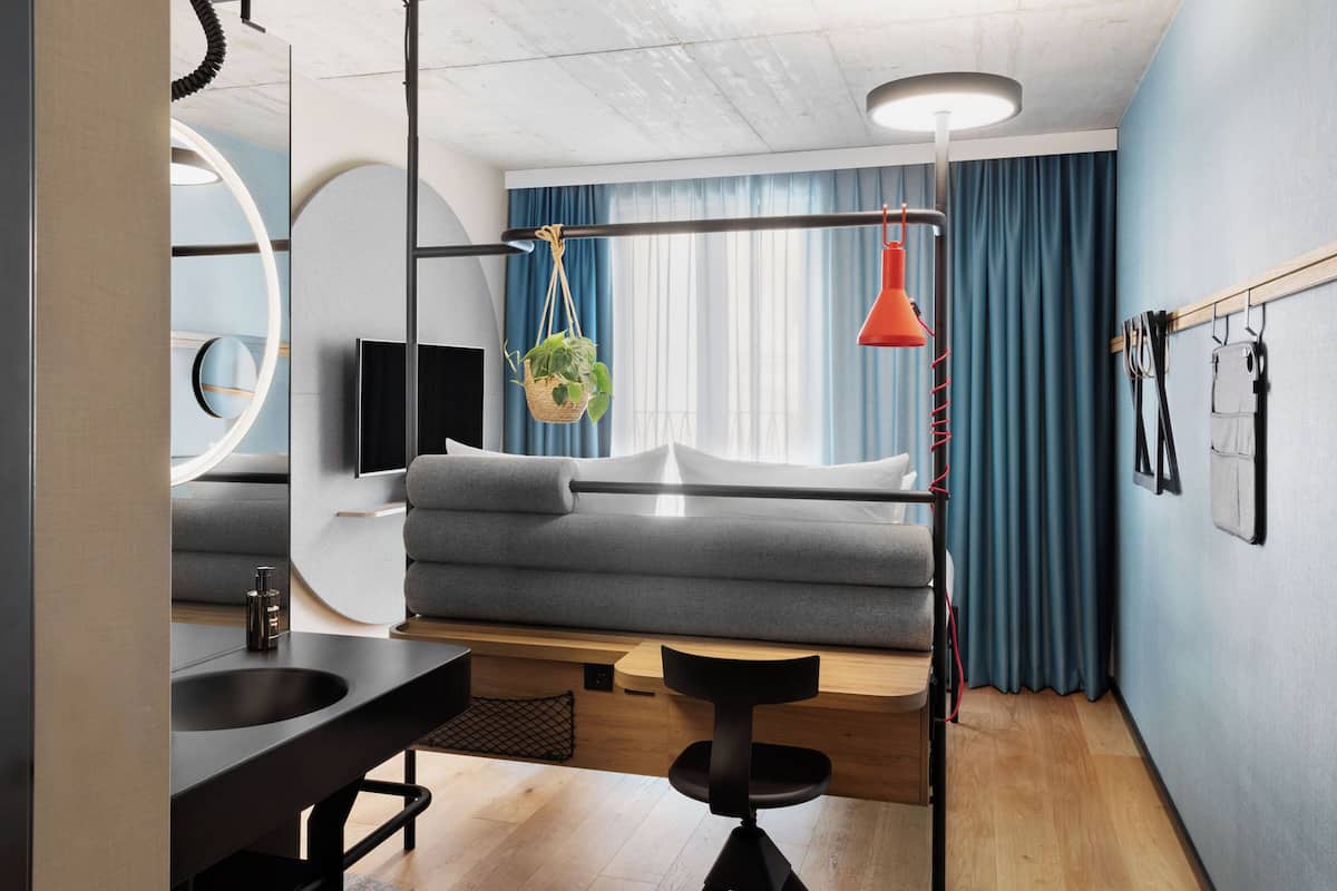 A modern room with a grey sofa, a black desk with a sink, a hanging plant, and a red pendant light.