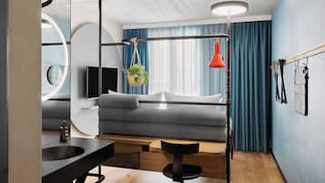 A modern room with a grey sofa, a black desk with a sink, a hanging plant, and a red pendant light.
