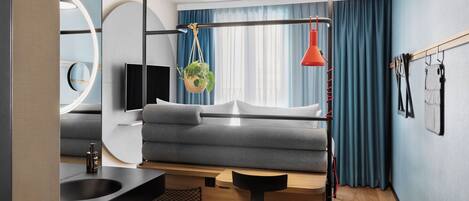A modern room with a grey sofa, a black desk with a sink, a hanging plant, and a red pendant light.