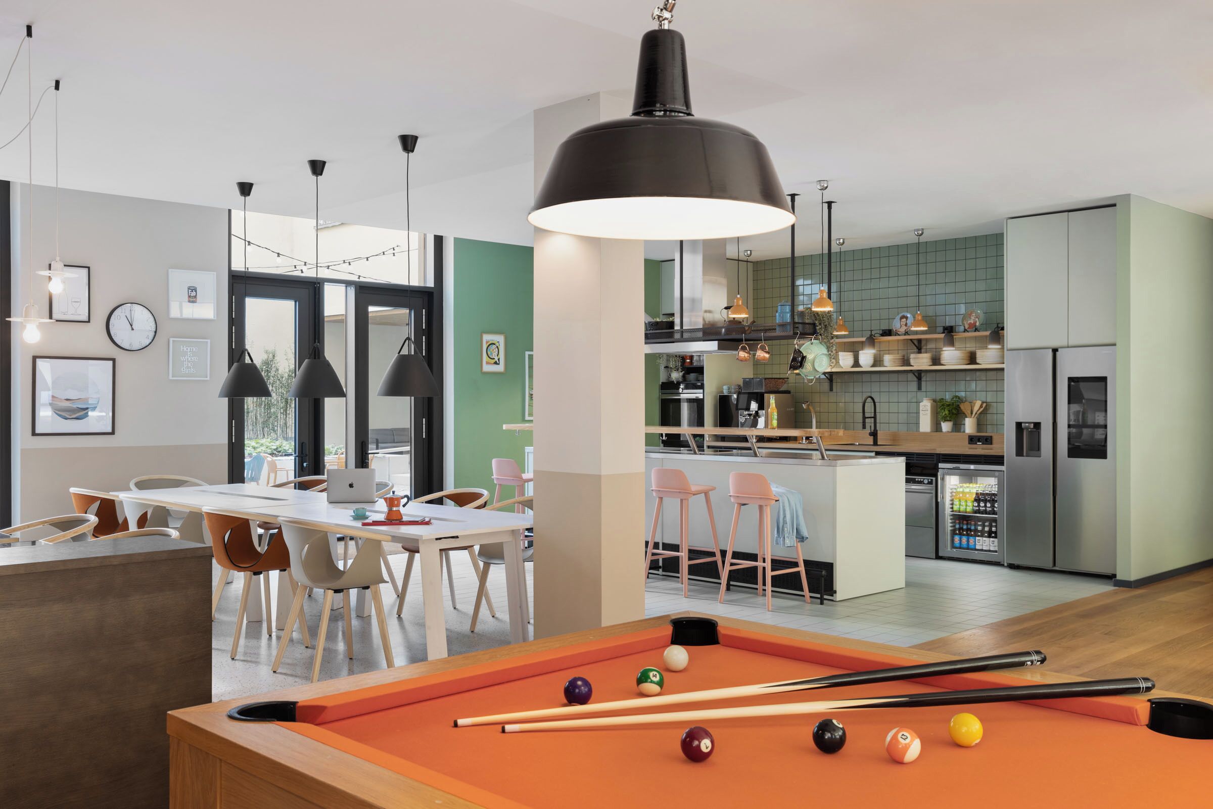 Una sala moderna con mesa de billar, comedor, cocina y vistas al exterior.