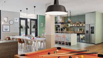 Una sala moderna con mesa de billar, comedor, cocina y vistas al exterior.