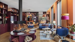 A modern living room with a fireplace, blue sofas, a coffee table, and a bookshelf filled with various items. - Stay KooooK Leipzig City – Online Check In (Leipzig)