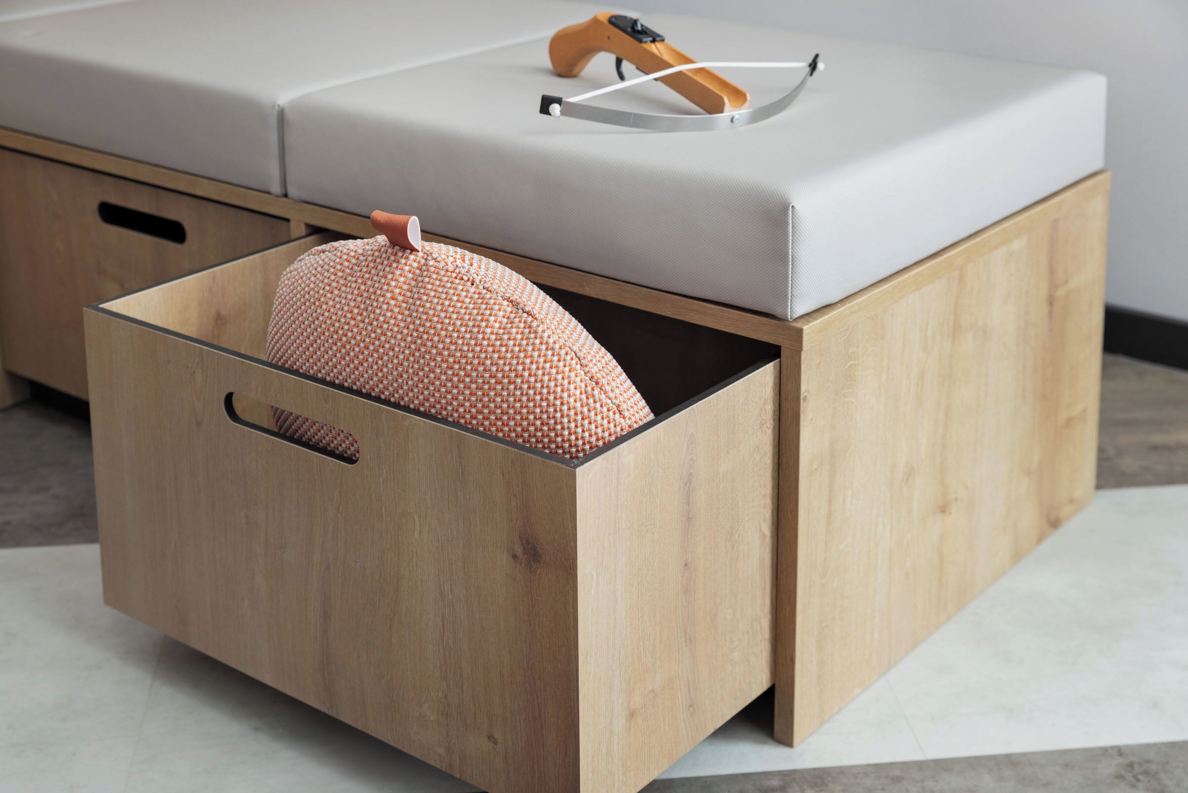 A wooden chest with a cushion inside, a wooden bench with a cushion, and a pair of sunglasses on the bench.
