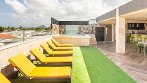 Eine Dachterrasse mit gelben Liegestühlen, einem kleinen Pool und einer Bar.