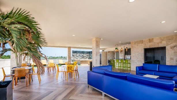 Ein großzügiger Außenbereich mit blauen Sofas und gelben Sesseln, einer großen Palme und Blick auf die Stadtlandschaft.