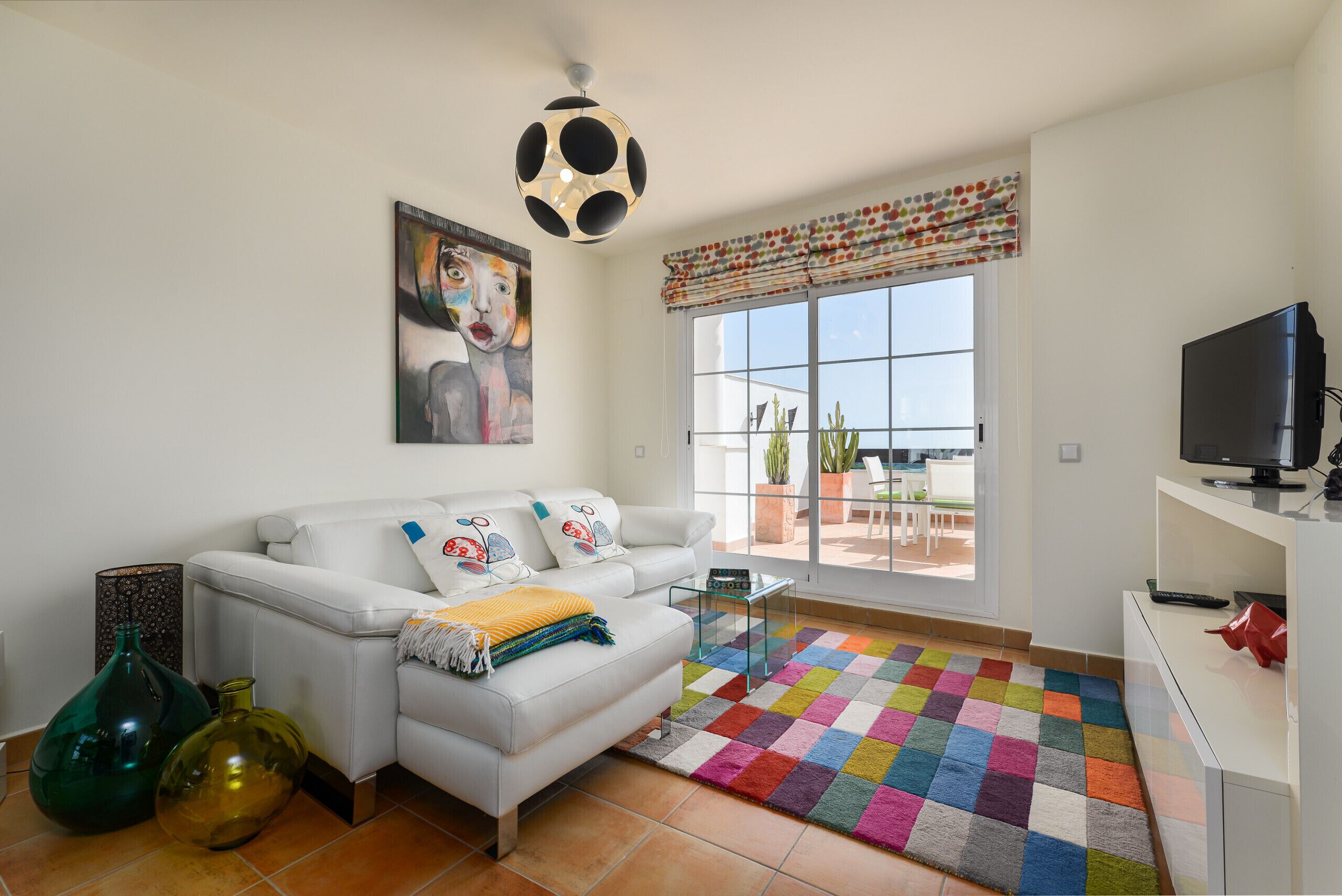 Una sala de estar moderna con un sofá blanco, un tapete colorido y un amplio ventanal con vistas al exterior.