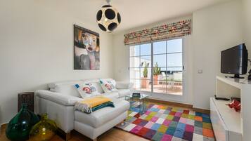 Una sala de estar moderna con un sofá blanco, un tapete colorido y un amplio ventanal con vistas al exterior.