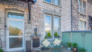 A stone building with large windows, a green door, and a small outdoor seating area with chairs and a table. - 2 bedroom accommodation in Colwyn Bay (Colwyn Bay)
