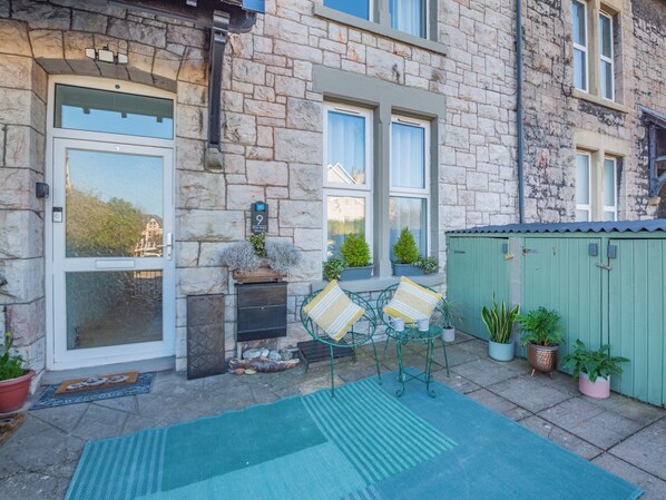 A stone building with large windows, a green door, and a small outdoor seating area with chairs and a table. - 2 bedroom accommodation in Colwyn Bay (Colwyn Bay)