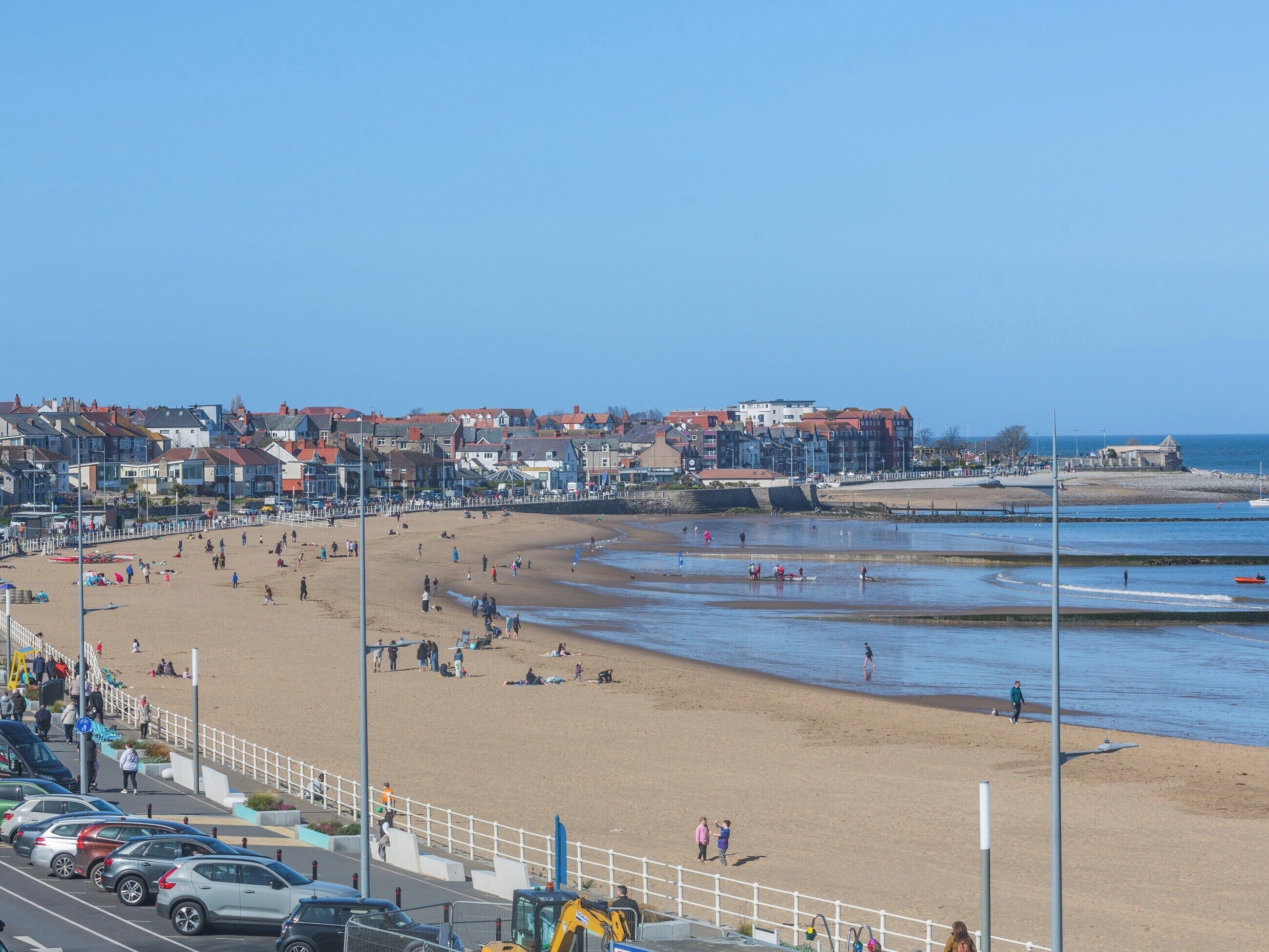 A beach with people, cars, and buildings in the background.