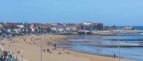 A beach with people, cars, and buildings in the background.