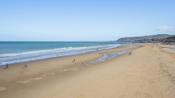A wide sandy beach with gentle waves, a clear sky, and a distant town on a hill. - 2 bedroom accommodation in Colwyn Bay (Colwyn Bay)