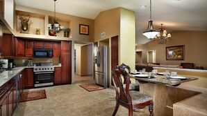Una cocina amplia con electrodomésticos modernos, un comedor con una silla de madera y una sala de estar con sofá y un cuadro.