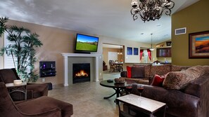 Uma sala de estar com lareira, televisão e um espaço de jantar ao fundo.