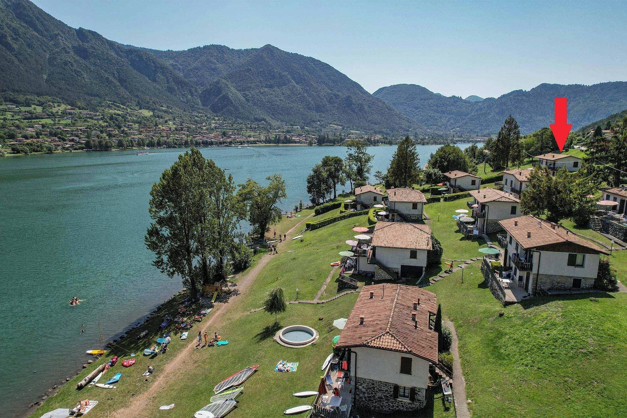 A lakeside village with houses, a swimming area, and a mountain backdrop.
