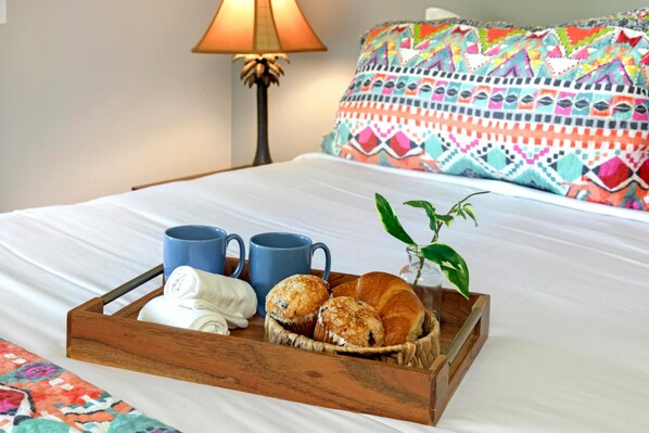 Ein Bett mit einem Holftablett, das Croissants, zwei blaue Tassen und ein zusammenrolltes weißes Handtuch zeigt.