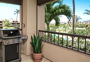 En balkon med grill, en potteplante og udsigt til en pool og palmer.