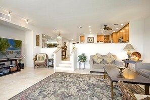A spacious living room with a large flat-screen TV, a sofa, a coffee table, and a patterned rug.