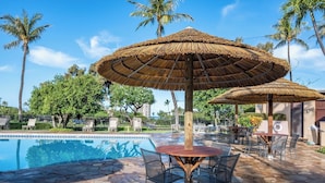A pool area with a stone floor, lounge chairs, and thatched umbrellas.
