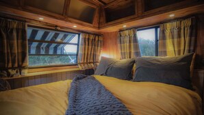 A cozy bedroom with a large bed, wooden walls, and two windows with curtains.