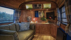 A cozy cabin interior with a wooden ceiling, a sofa, a small table with a lamp, and a television.