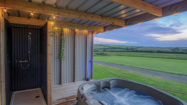 A hot tub with a view of a green field, a wooden door, and a shower area.